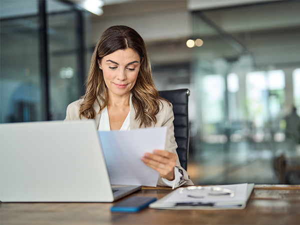 Business woman working in office and looking down at paper. Laptop is sitting on top of desk.